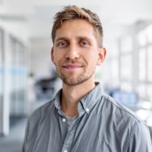 Close-up portrait of businessman looking at camera while standing in office. Confident male business executive at coworking office space.